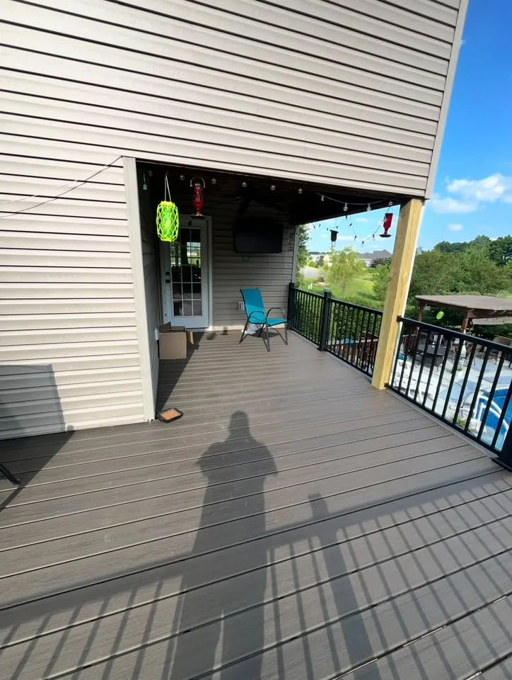 Covered gray deck area with dark railings beside the home