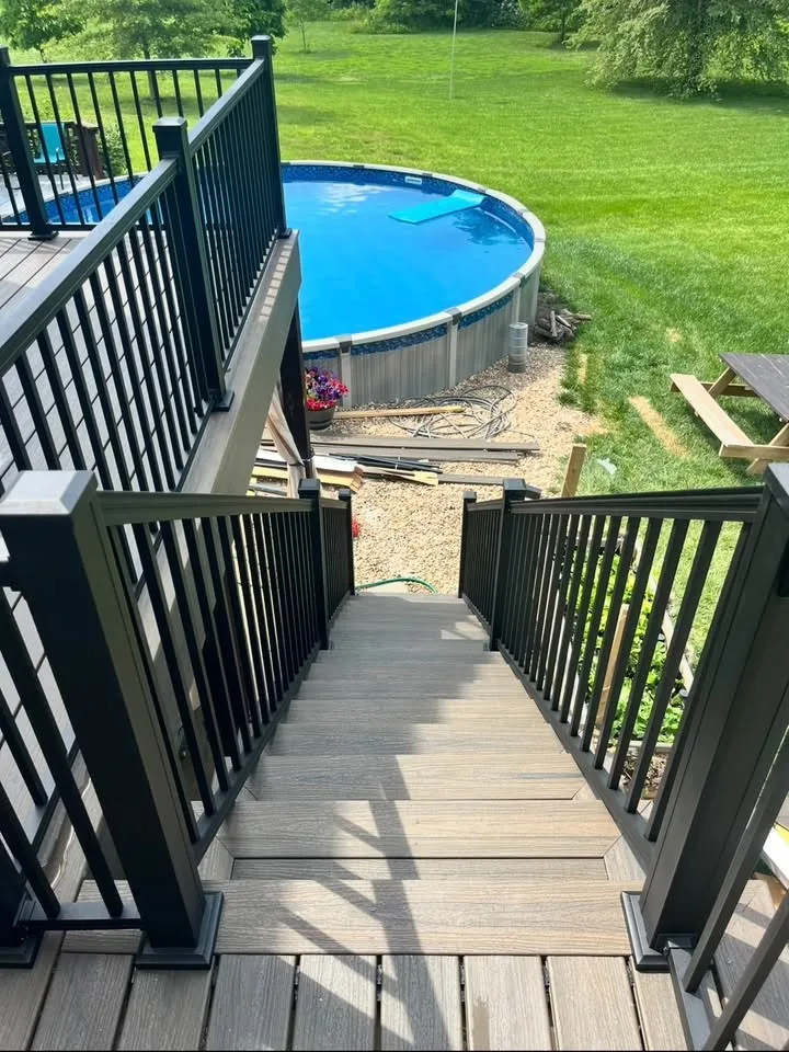 Gray deck stairs with dark railings leading toward an above-ground pool